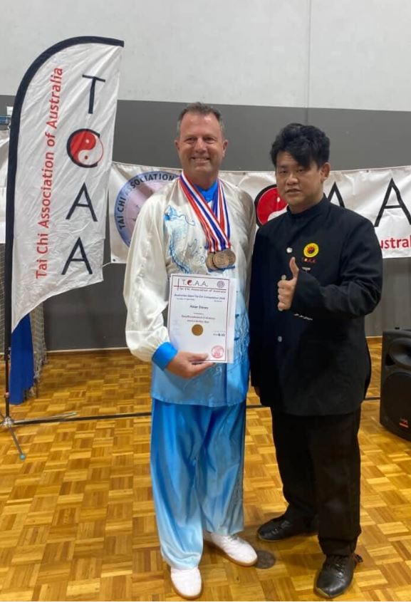 Peter Davey wearing his medals and holding his certificate beside a Tai Chi Association of Australia official