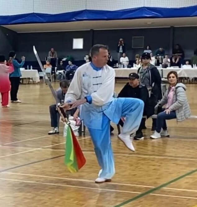 Peter Davey on one leg with the sabre raised, its red, yellow and green tassel hanging, competing in blue and white silk