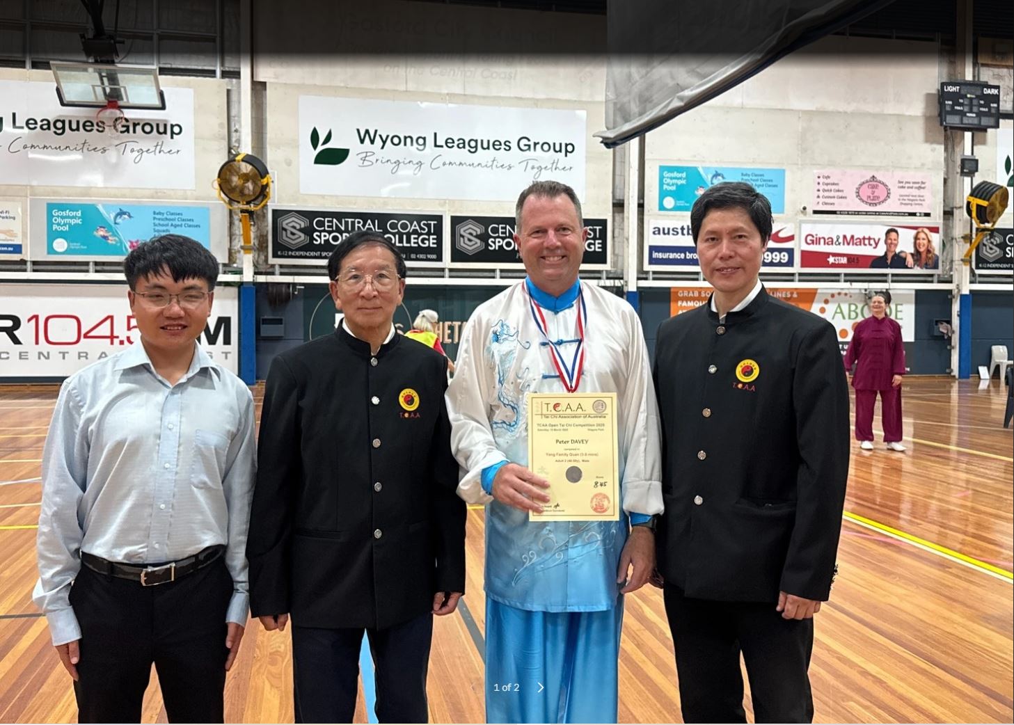 Peter Davey in blue and white silk holding his certificate and wearing his medal, standing with three Tai Chi Association of Australia officials