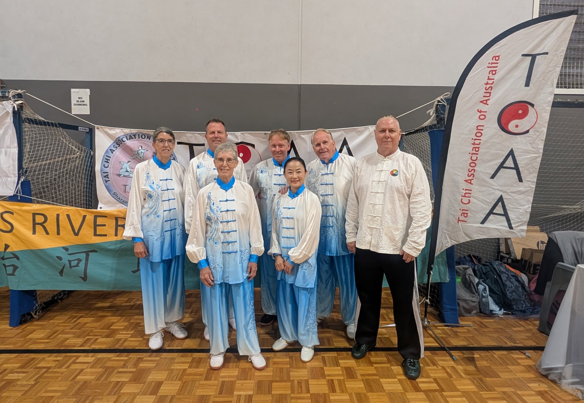 The Newcastle Tai Chi team in blue and white silk uniforms with Peter Davey, standing in front of Tai Chi Association of Australia banners